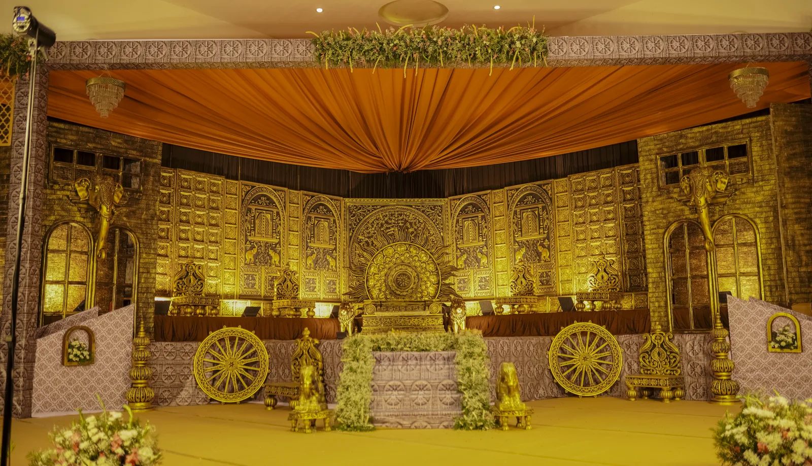 A full wedding hall decorated with a carved gold backdrop and a draped ceiling